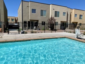A swimming pool with clear blue water, surrounded by a concrete deck and a black fence.