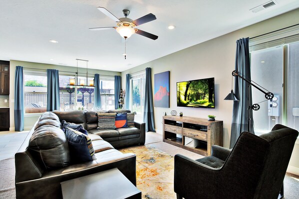 A modern living room with a sofa, armchairs, a coffee table, a TV, and a ceiling fan.