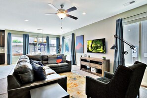 A modern living room with a sofa, armchairs, a coffee table, a TV, and a ceiling fan.