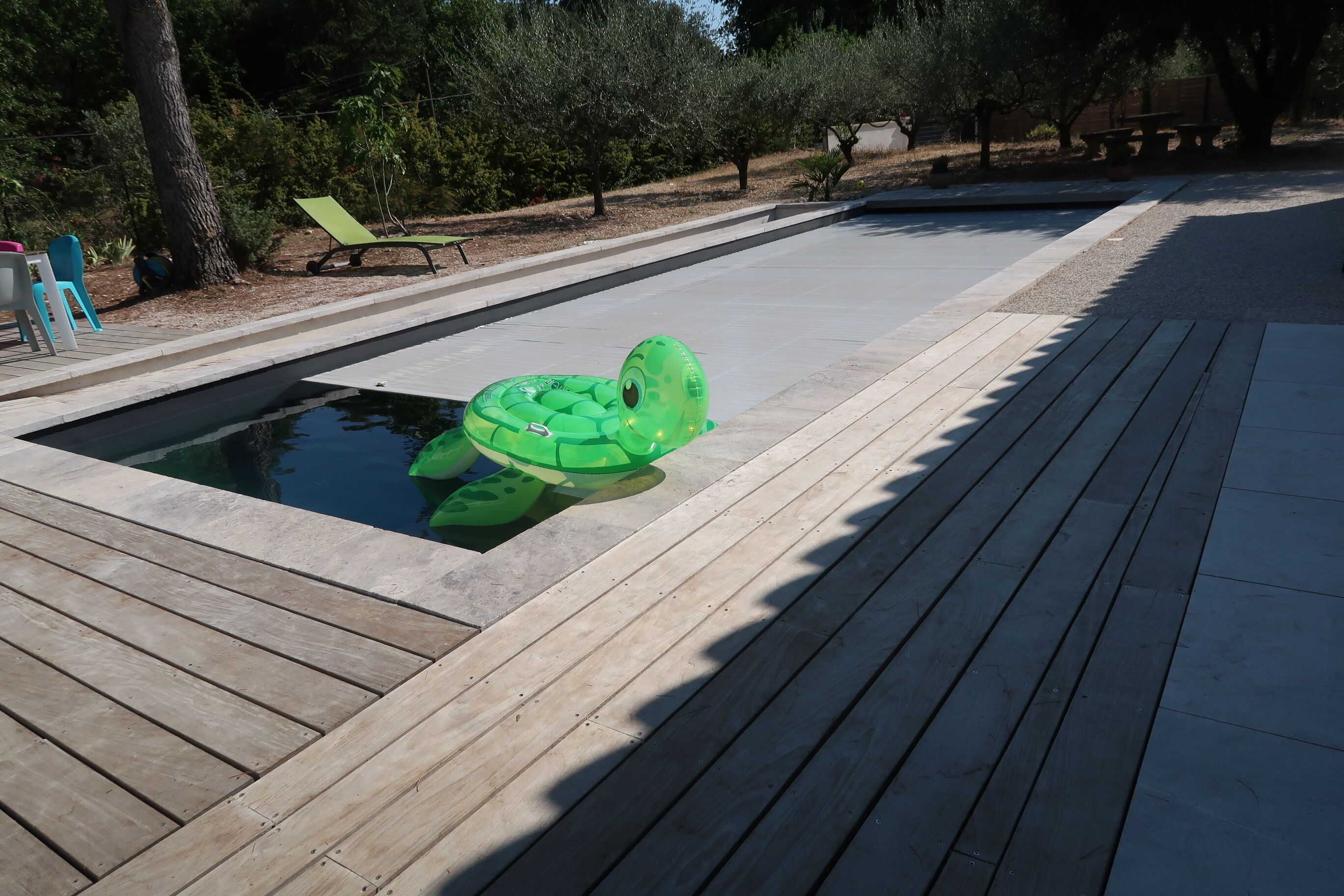 Une piscine avec un flotteur gonflable vert, une terrasse en bois et des sièges d’extérieur.