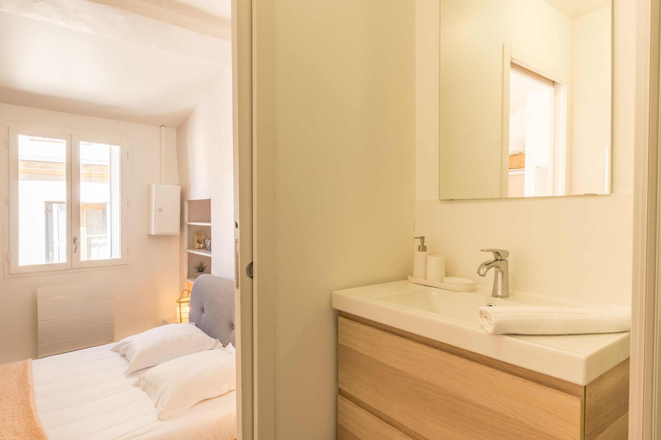 Ein Schlafzimmer mit Bett, Nachttisch, Kleiderschrank und einem Badezimmer mit Waschbecken und Spiegel.