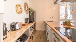 Cocina compacta con tostadora, hervidor y lavabo. Se observan adornos en la pared y una planta en maceta.