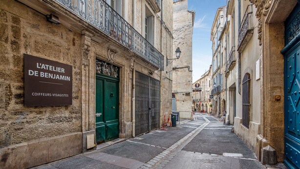 Una calle estrecha flanqueada por edificios, uno de los cuales muestra un cartel que dice 'L'Atelier de Benjamin'.