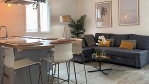 Una cocina moderna con una isla central, sillas blancas y un sofá gris con cojines.