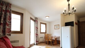 Ein gemütlicher Wohnbereich mit einer Couch, einem Esstisch mit Stühlen, einem Kühlschrank und einer Chandelüster.