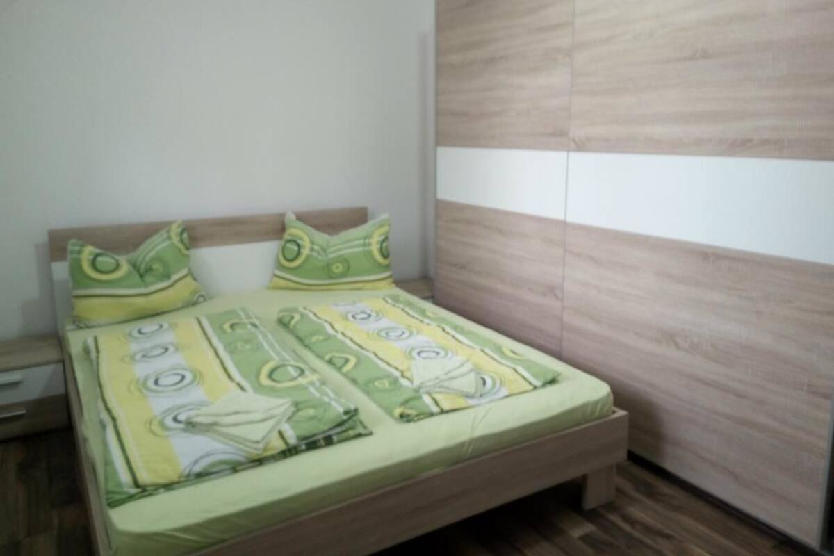 A bedroom with a bed, a wooden wardrobe, and a nightstand.