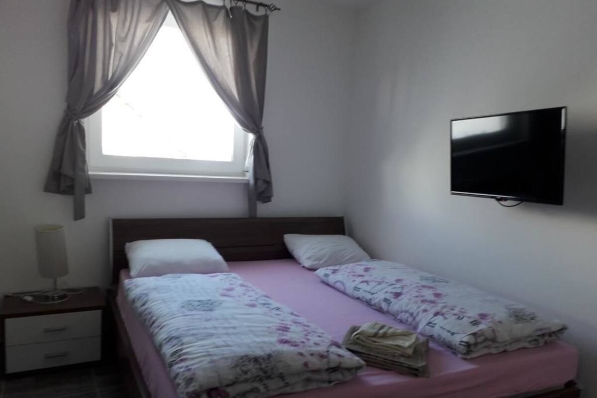 A bedroom with a bed, a nightstand, a TV, and a window with curtains.