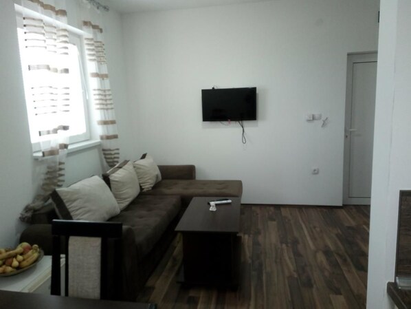 A living room with a brown sofa, a small table, and a flat-screen TV mounted on the wall. - Villa Mozart (Raška)