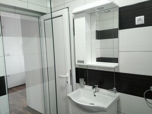 A bathroom with a glass shower enclosure, a white sink with a mirror above it, and black and white tiled walls. - Villa Mozart (Raška)