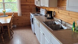 A kitchen with wooden walls, white cabinets, a double sink, and a stove.