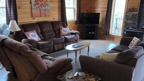 A cozy cabin interior with a wooden ceiling, a fireplace, a sofa set, and a television.