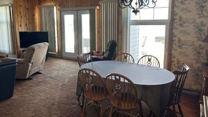 Un coin repas avec une table ronde, des chaises en bois, un ventilateur de plafond et une grande fenêtre avec des rideaux.