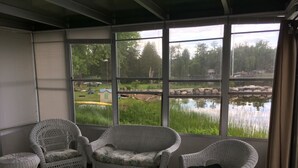 Une pièce meublée de mobilier en osier, dotée de grandes fenêtres et offrant une vue sur un étang.