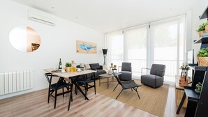 En moderne stue med spiseområde, store vinduer, et rundt spejl og udsigt til det fri.