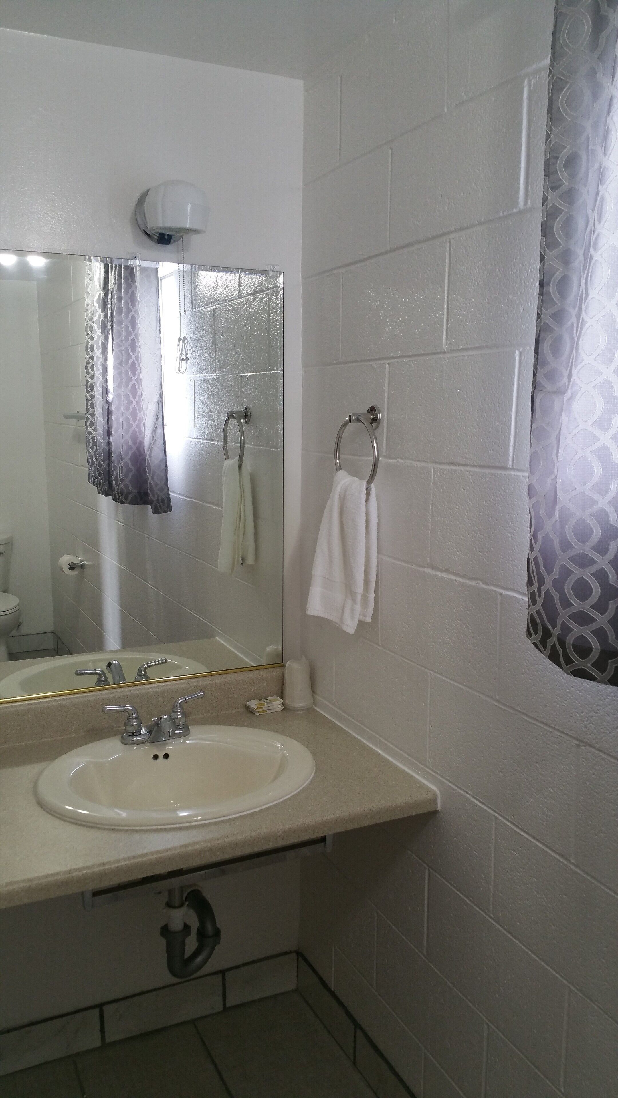 Un baño con lavamanos, espejo, toallero y cortina de ducha.