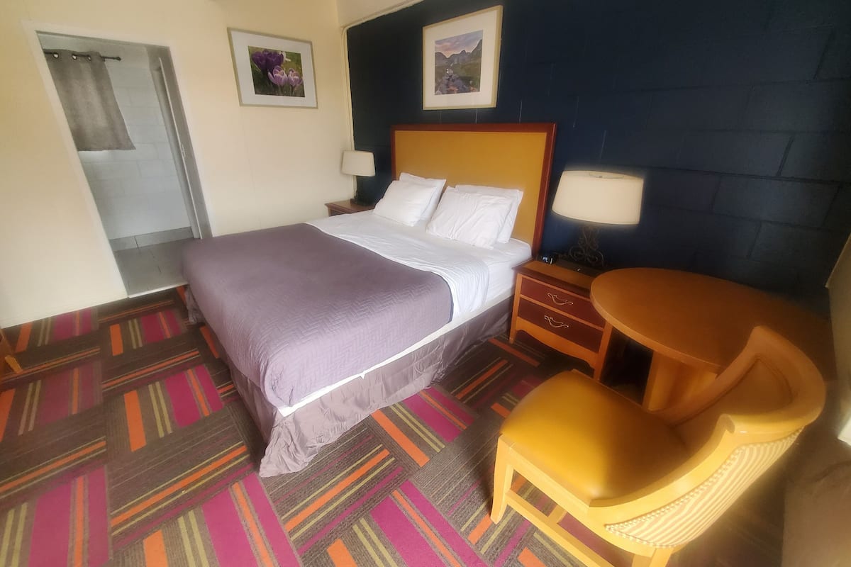 A hotel room with a bed, a chair, a nightstand, two wall-mounted lamps, and two framed pictures.