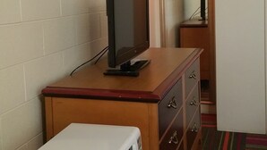 A hotel room with a television on a wooden dresser, a white suitcase, and a mirror on the wall. - Thunder Bird Motel (Mountain Home)