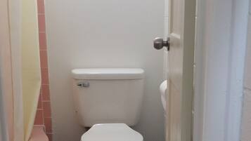 A small, narrow bathroom with a white toilet, a pink bathtub, and a tiled floor.