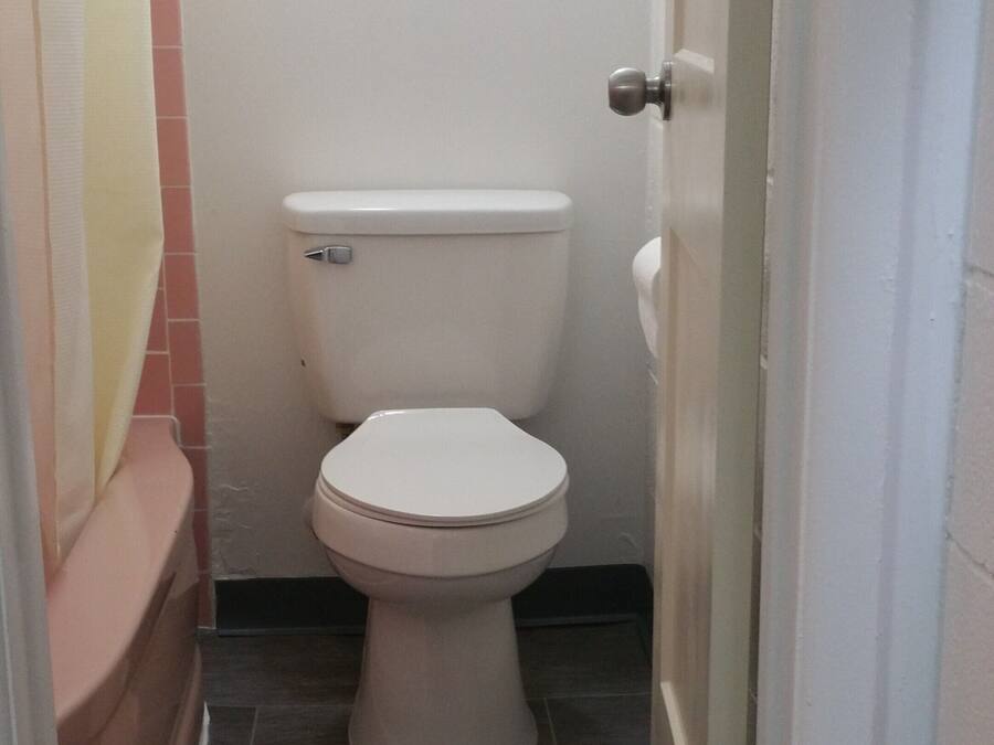 A small, narrow bathroom with a white toilet, a pink bathtub, and a tiled floor.