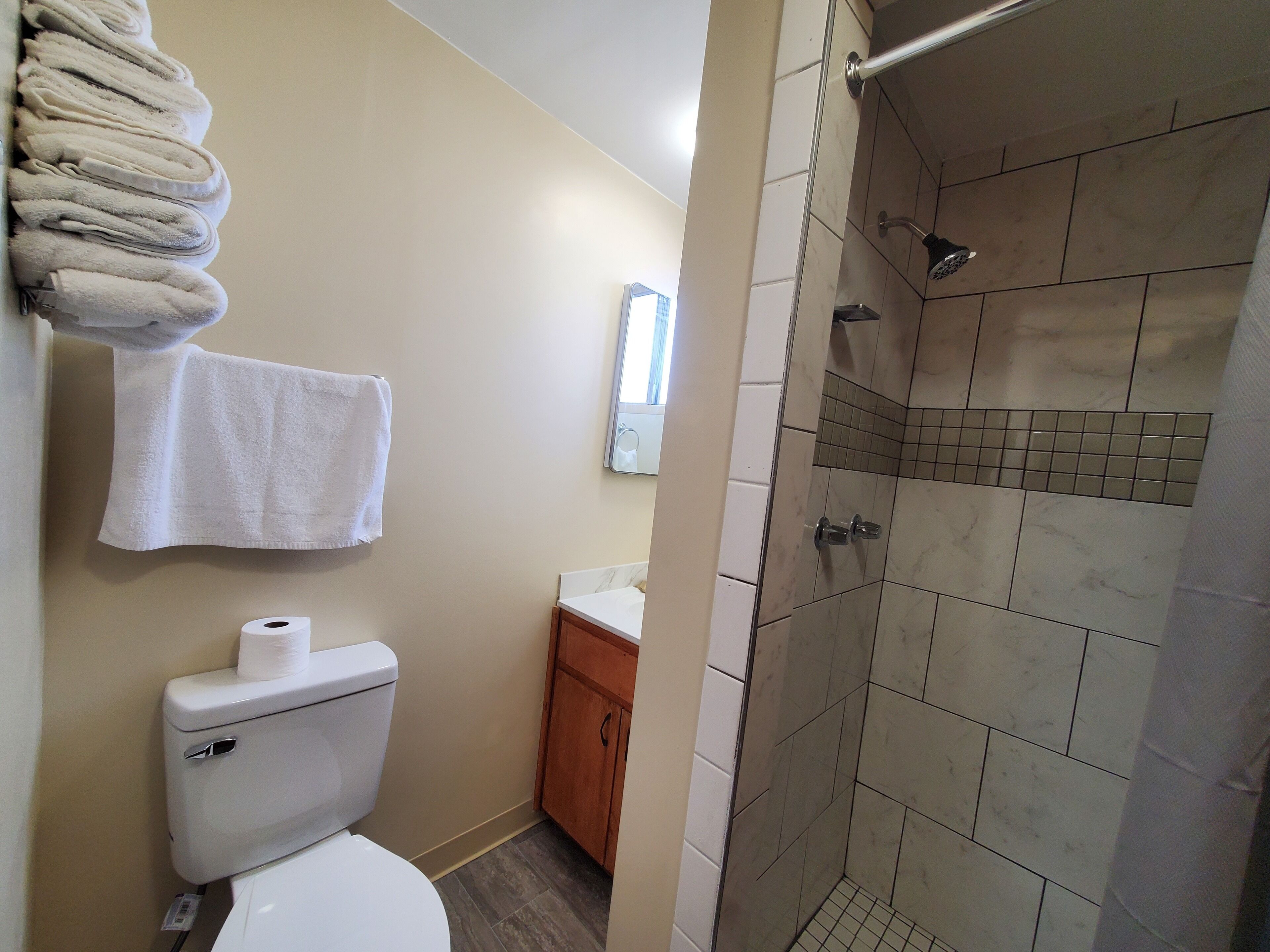 Une salle de bain comprenant des toilettes, un lavabo, un porte-serviettes avec des serviettes et un espace douche avec des murs carrelés.