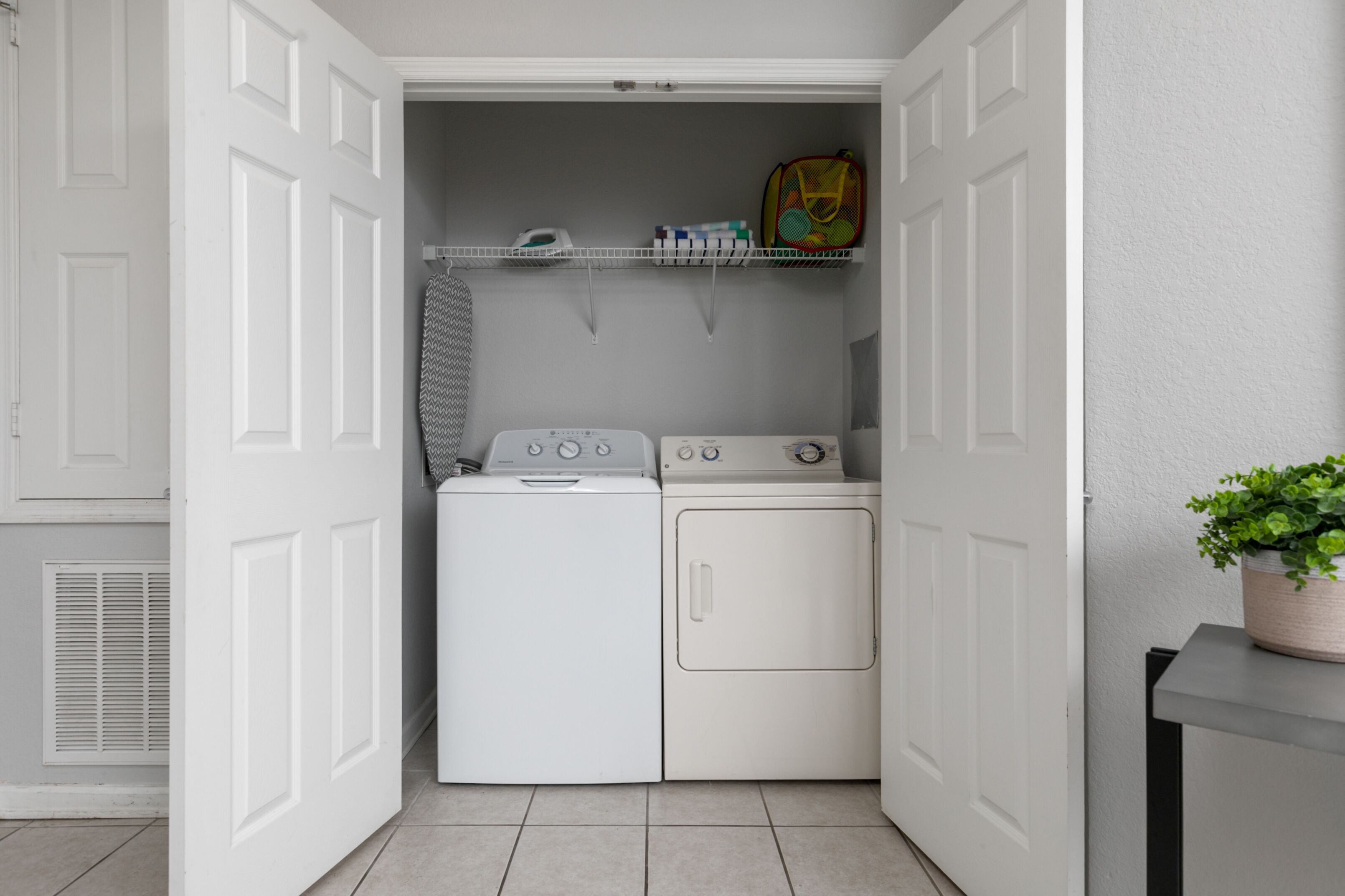 Une buanderie équipée d’un lave-linge et d’un sèche-linge, d’une étagère contenant des produits de lessive et d’une plante en pot.
