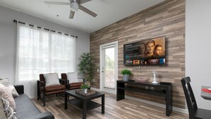 A modern living room with a wooden accent wall, a flat-screen TV, a sofa, a coffee table, and a dining area.