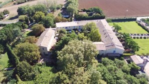 Vista aérea de un edificio grande y rectangular con techo plano, rodeado de vegetación densa y campos.