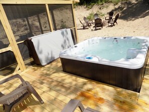 A hot tub on a wooden deck with a covered seating area and a view of a sandy beach.