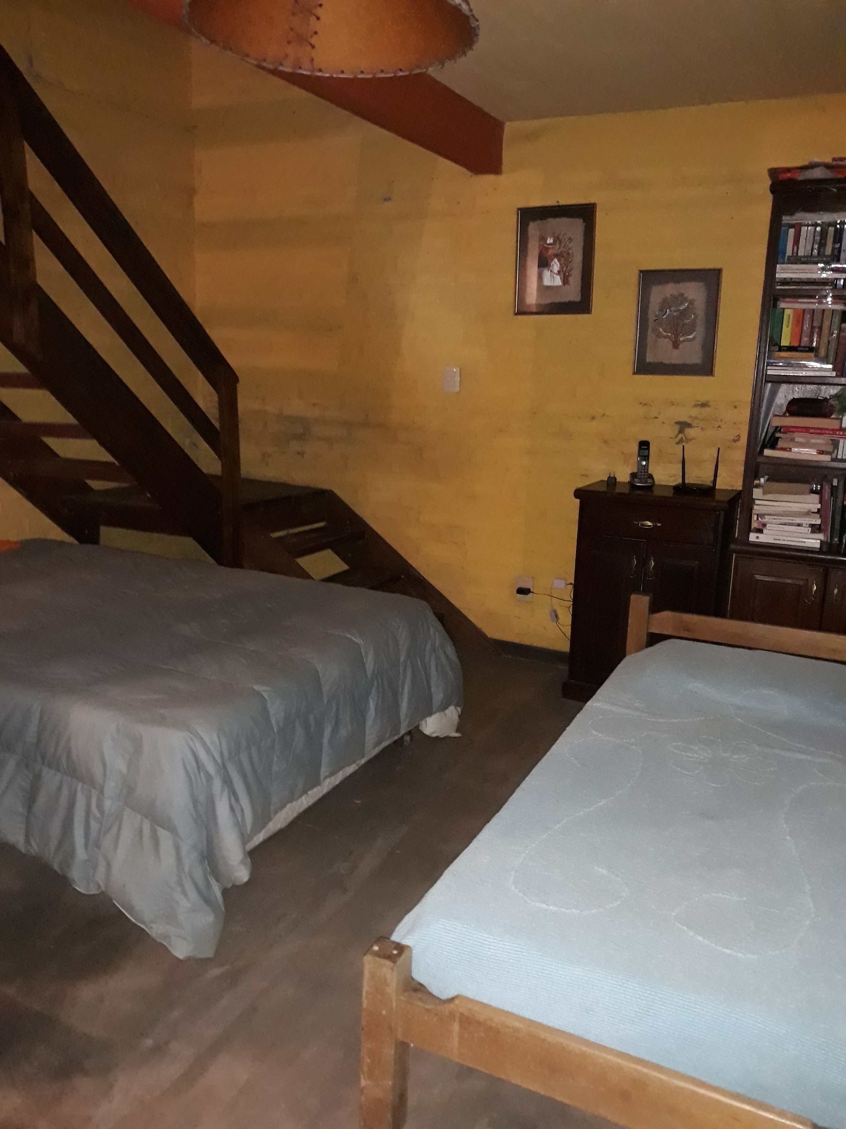 A room with two beds, a wooden staircase, a bookshelf, and a small desk.