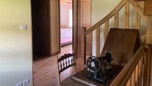 Un escalier en bois, une machine à coudre posée sur une table, une rambarde en bois et un lit dans la pièce adjacente.