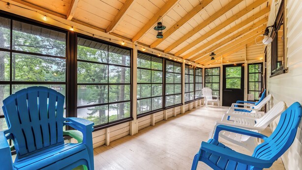 Une véranda couverte avec des poutres en bois, de grandes fenêtres et des chaises en plastique.