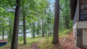 Une zone boisée avec un sentier de terre menant à un chalet situé au bord d’un lac.