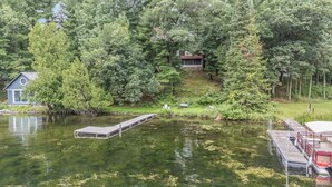 Un chalet au bord du lac, doté d’un quai s’avançant dans l’eau, et entouré d’une forêt dense.