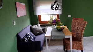 Una habitación con una pared verde, un sofá con un cojín estampado, una silla de mimbre, una mesa con un cuenco de fruta y una araña.