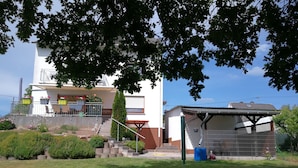 Una casa de dos pisos con un balcón, un porche cubierto y un pequeño jardín.