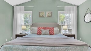 A bedroom with a bed, two bedside tables, a nightstand, a window with curtains, and wall art.