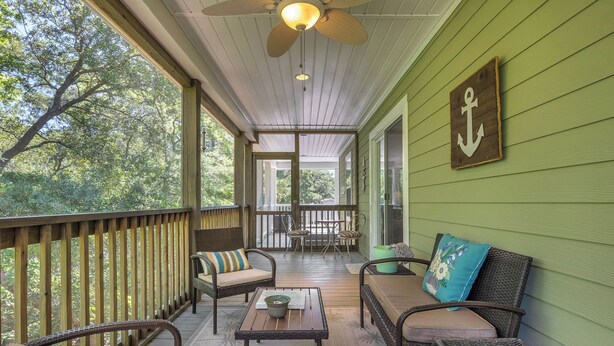 A covered porch with wicker furniture, a ceiling fan, and a view of trees.