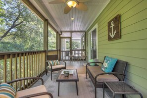 Eine überdachte Veranda mit Korbmöbeln, einem Deckenventilator und Blick auf Bäume.