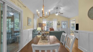 A dining area with a wooden table, white chairs, a chandelier, and a view of the outdoors.