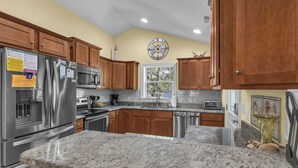 A kitchen with granite countertops, stainless steel appliances, wooden cabinets, and a clock on the wall.