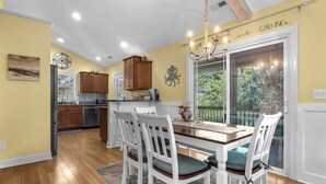 A dining area with a wooden table and white chairs, a chandelier, and a view of the outdoors through a glass door.