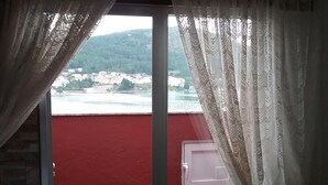 Une pièce avec un mur rouge, une fenêtre avec des rideaux et une vue sur une étendue d’eau et de la verdure.