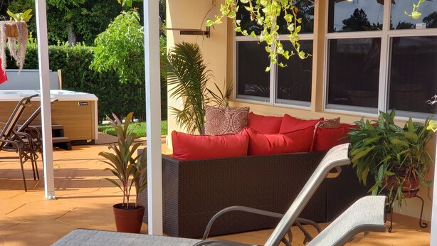 A covered outdoor seating area with a wicker sofa and metal chairs.