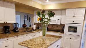 A kitchen with white cabinets, granite countertops, a built-in oven, and a central island with a vase of flowers.