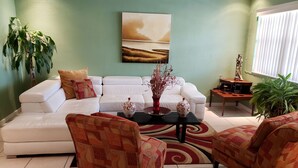 A living room with a white sofa, patterned armchairs, a coffee table with decorative vases, and a painting on the wall.