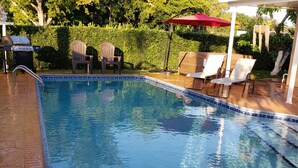 A swimming pool with a tiled edge, surrounded by lounge chairs and a barbecue grill.