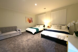 A bedroom with two beds, a sofa, a painting, and a lamp.