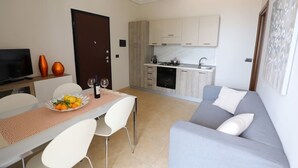 Una sala moderna con un sofá gris, una mesa de comedor con sillas, una zona de cocina con armarios y un televisor sobre un mueble.