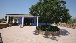 Una casa con un porche techado, un árbol en el centro y un muro de piedra.