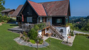 A two-story wooden house with a red roof, a wooden deck, and a staircase leading to a balcony.